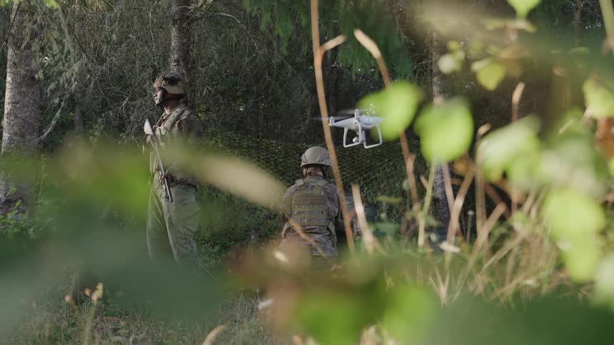 A soldier is flying a drone by the trees