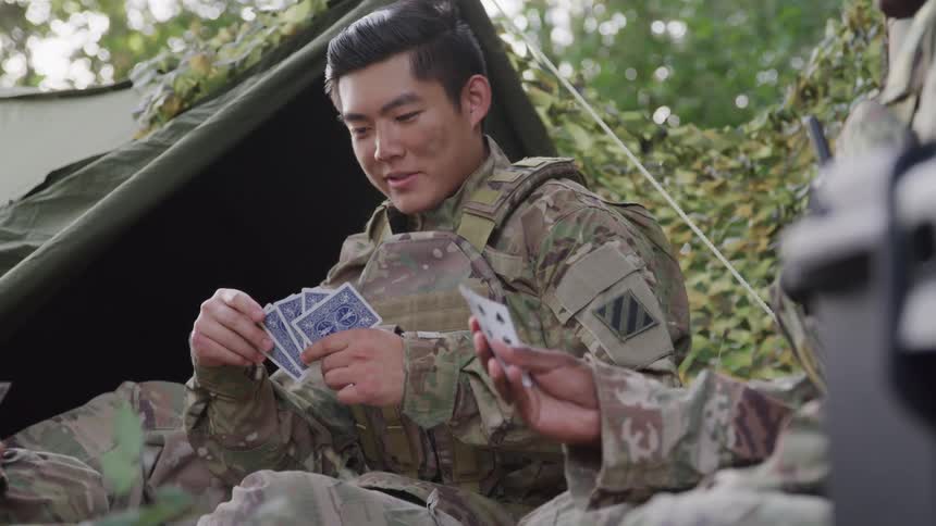 Military officers sit on the jungle floor at midday playing a card game