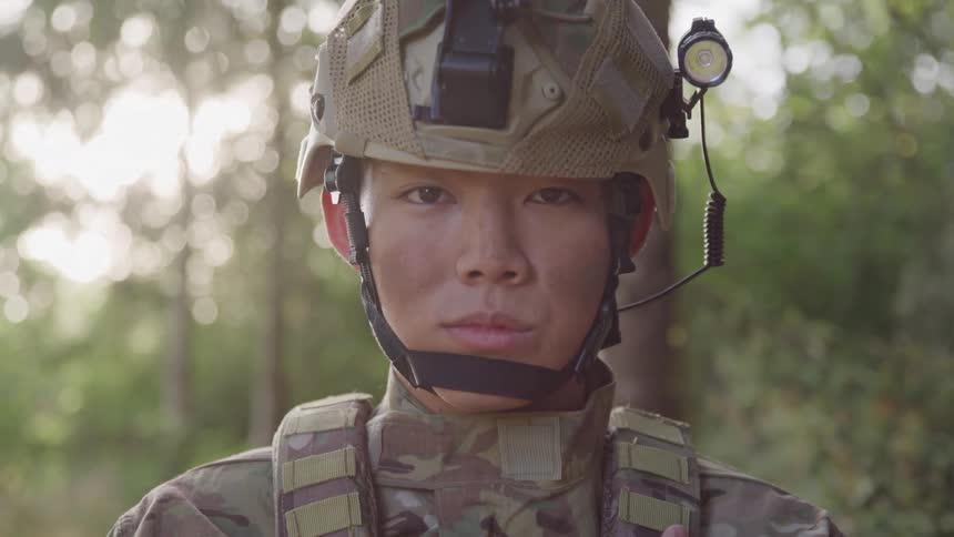 A military officer wearing helmet gear stands in the forest jungle at midday