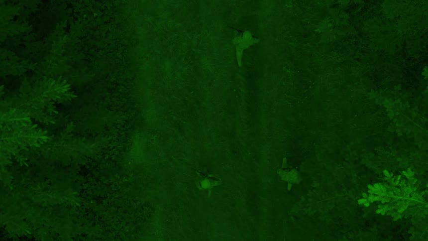 Three soldiers walking through a dense forest at night captured using night vision technology