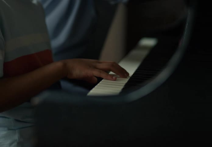 A boys hand is playing the keys of a dark piano in a dimly lit setting