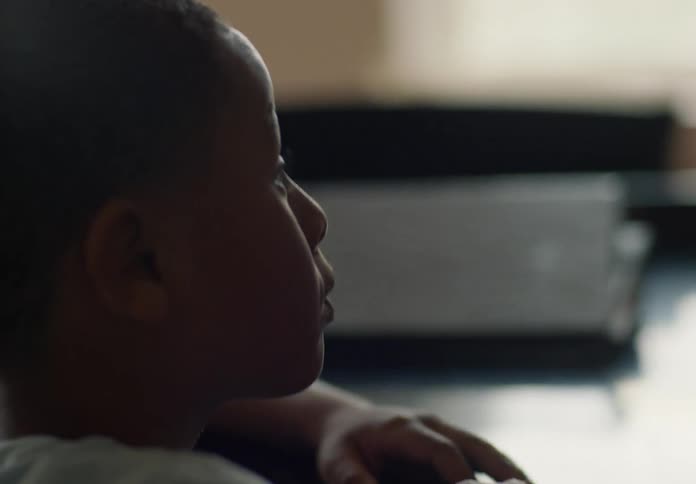 A black male child sits behind a desk picks up a folder and then tosses it to the side