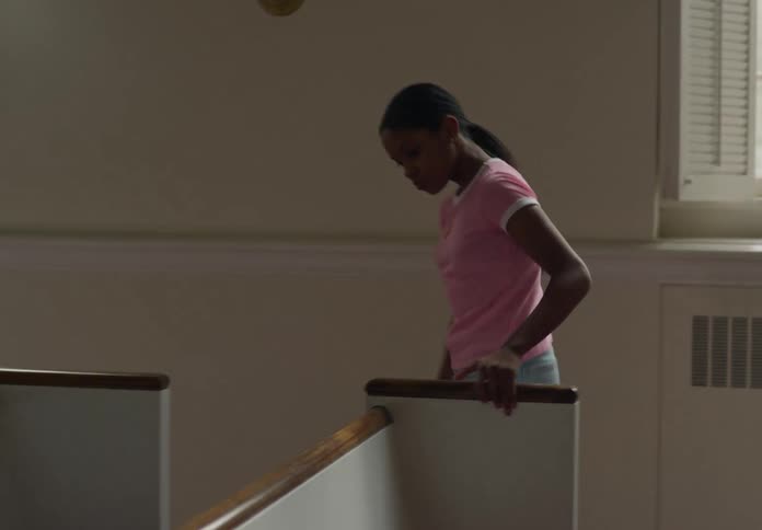 A young person in a pink shirt and denim shorts is organizing books in the pews of a church with large windows