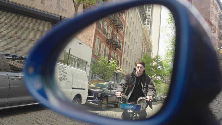 Man on a bicycle riding down a city street seen through a vehicles rearview mirror