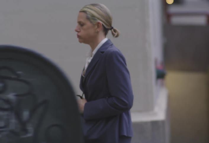 Woman in blazer walking hurriedly on city sidewalk