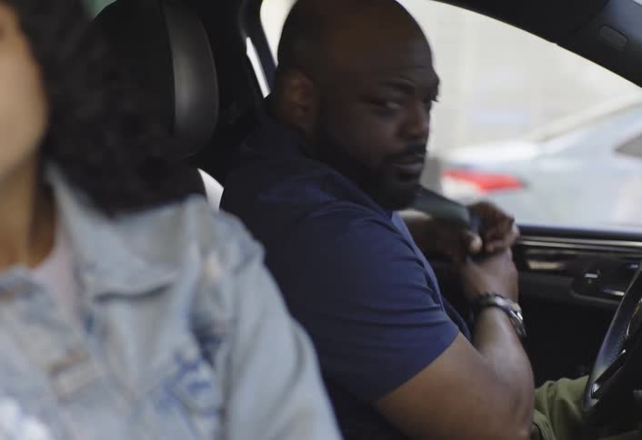 Father frowns while looking at his daughter while they sit in a parked car then they put on their seat belts