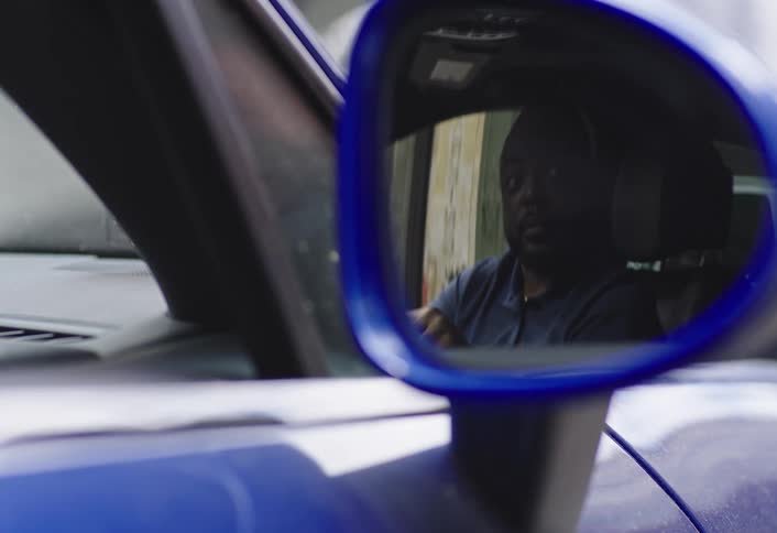A frustrated man is seen arguing inside a car his reflection captured in the drivers side mirror