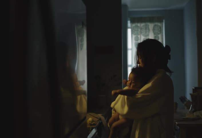A woman places something in the fridge then lovingly nurtures her infant