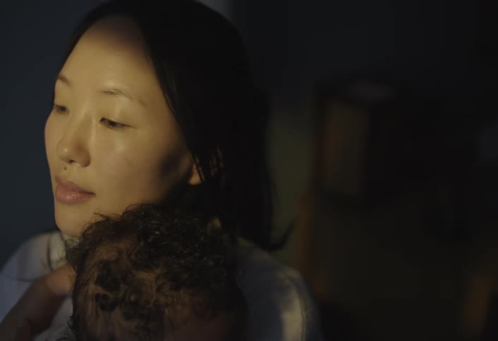 A woman gently holds a baby against her shoulder in a dimly lit room