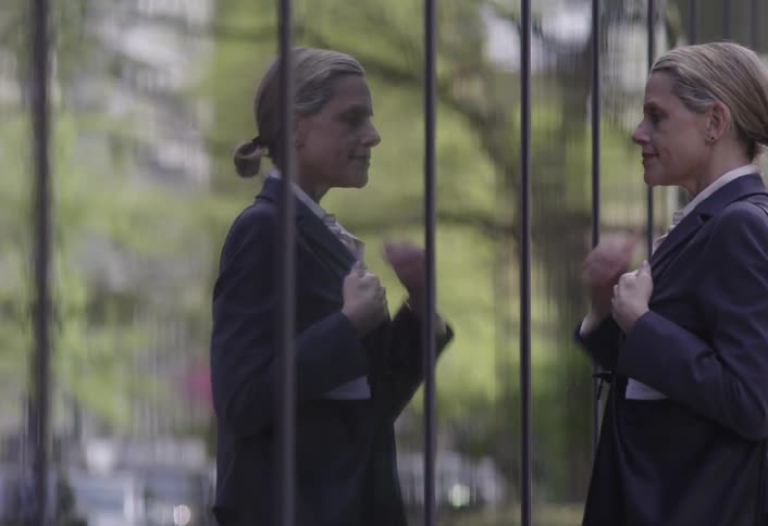 A woman checks her reflection in a tall glass building wall outside