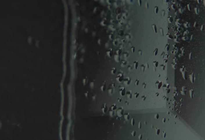 Water droplets trickle down a windowpane in a dark moody interior setting