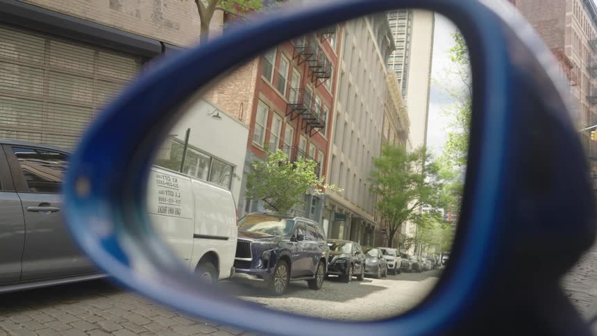 A man riding a bike is seen through a cars sideview mirror on a city street