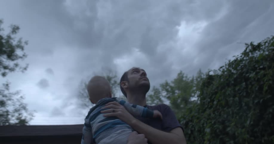 A man holding a baby in his arms in a backyard near some trees