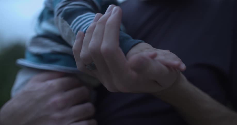 A man holding a baby in his arms gently holding the babys hand