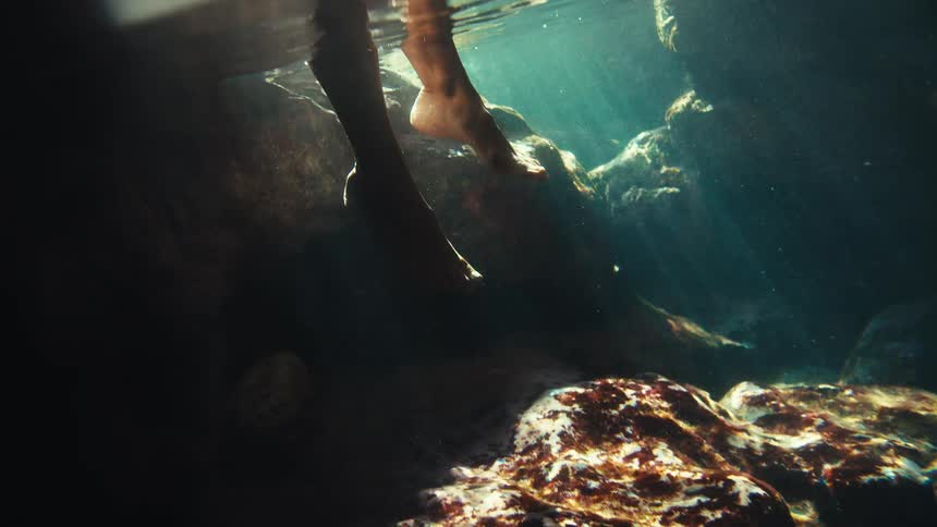 A person stepping into a lake with stones on the bottom