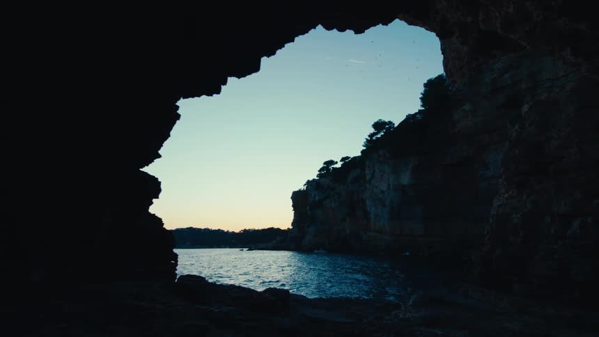 A woman walks from the ocean into the cave