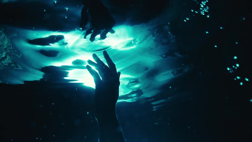 A persons arm moves underwater while swimming in the ocean at night