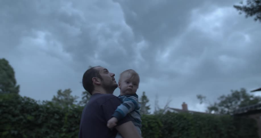 Father with son drinking on his lap in a cloudy outdoor setting