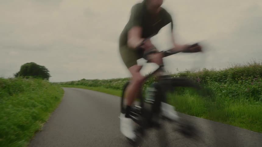 A woman cycles on a lonely road surrounded by grasses and bushes on both sides at midday
