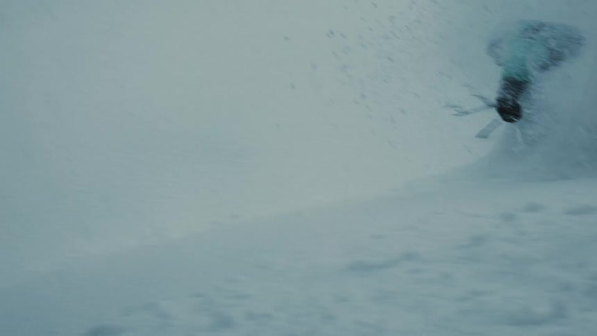 Person snowboards down a snowy slope passing leafless trees