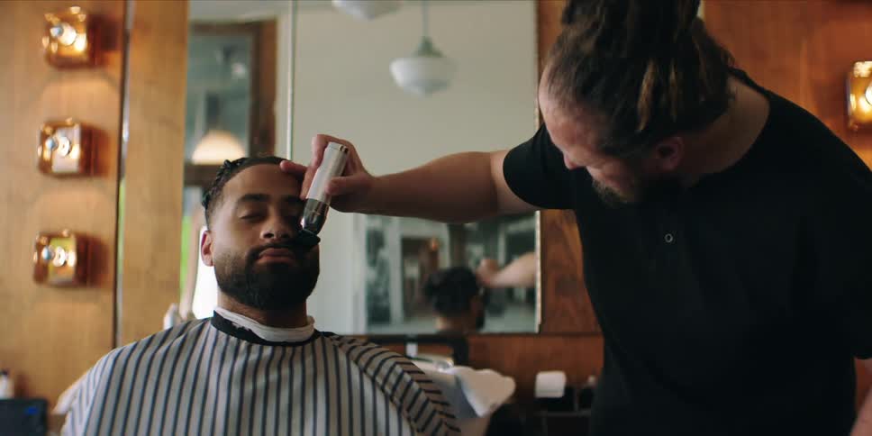 A barber is using clippers to trim a mans beard
