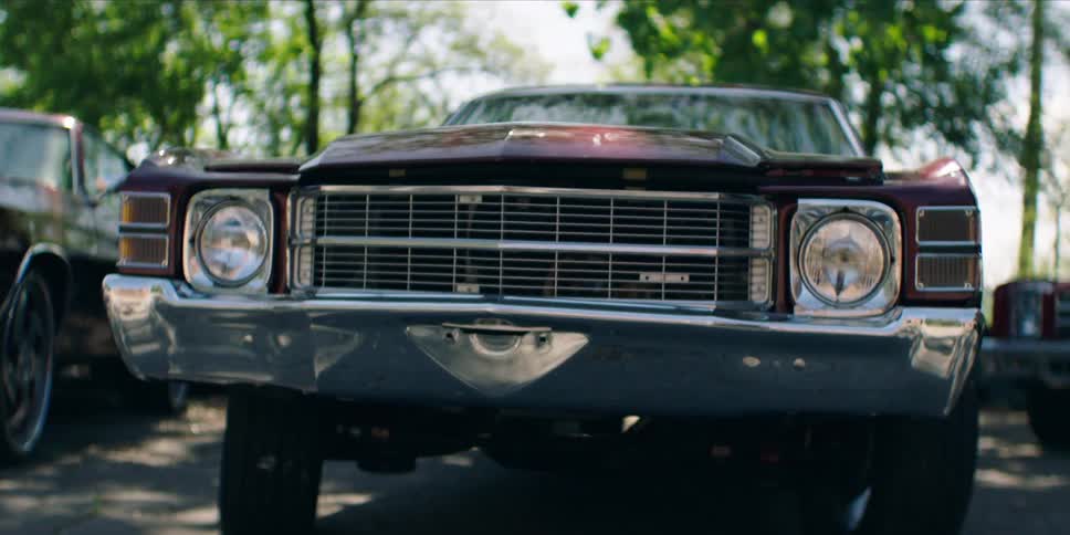 Classic cars sit in a parking lot near a garage on a sunny summer day