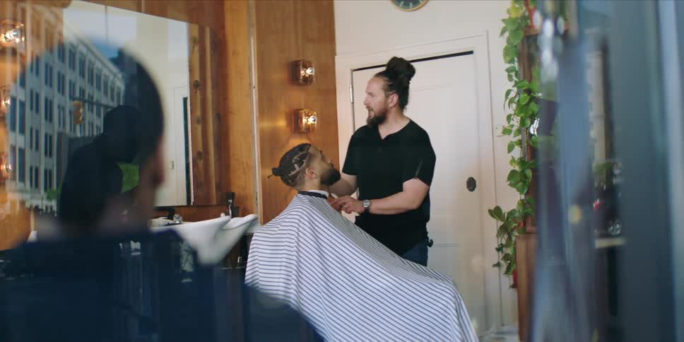 Barber works with one client while talking to another