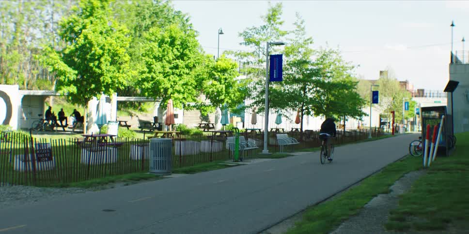 Cyclist rides along a street passing a park on a summer day