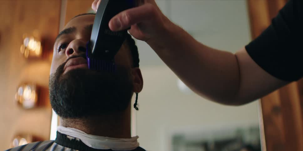 The barber leans forward shaving the mans beard