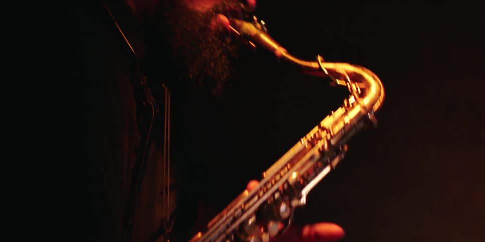 A man has his eyes closedd as he plays saxophone in a dark room