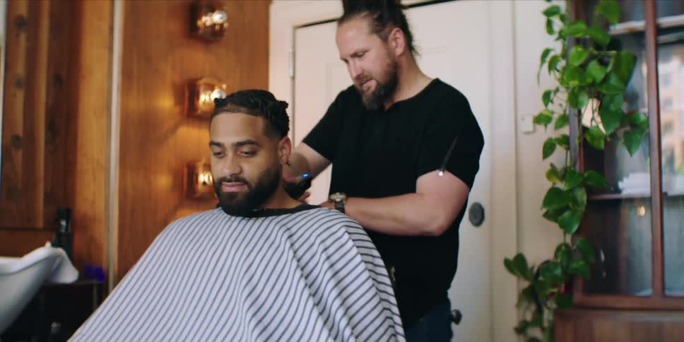 A barber giving a haircut to a man in a barbershop at midday with sunlight streaming in through the windows and the quiet buzz of clippers filling the room