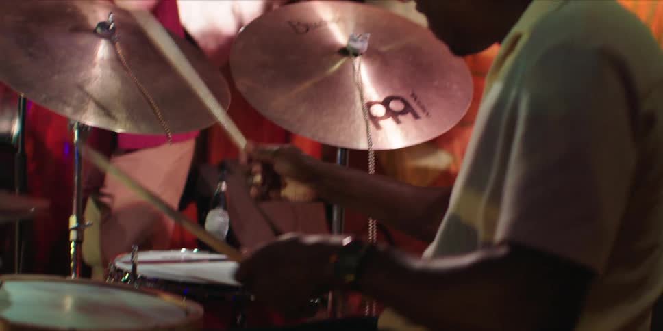 A drummer playing the drums energetically while another musician plays the guitar beside him on a stage