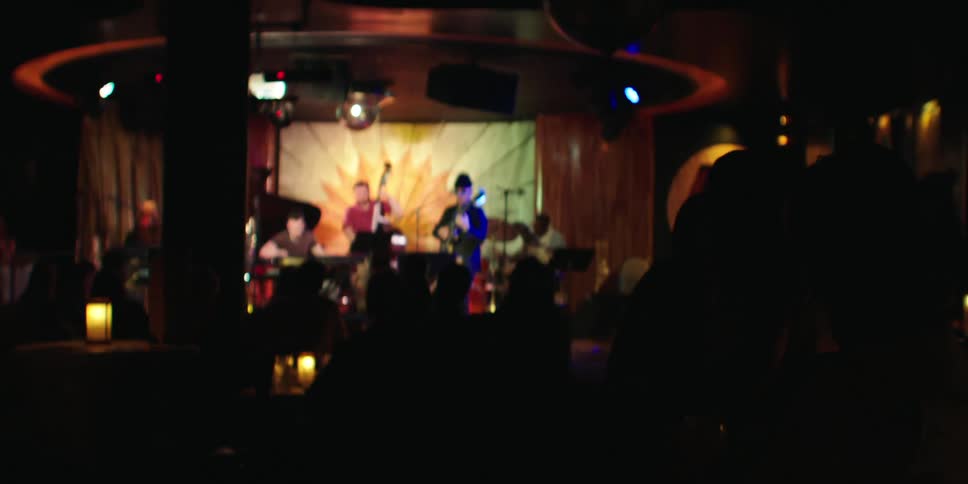 A live musical concert with musicians on stage playing various instruments creating an energetic atmosphere as the crowd enjoys the performance