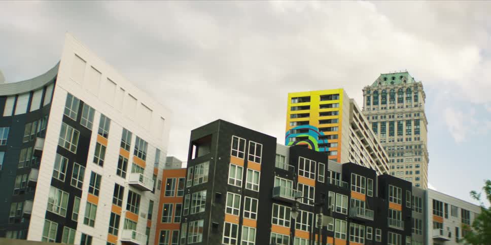 The facade of some black and white buildings has several windows and there is a yellow building with a blue design behind them