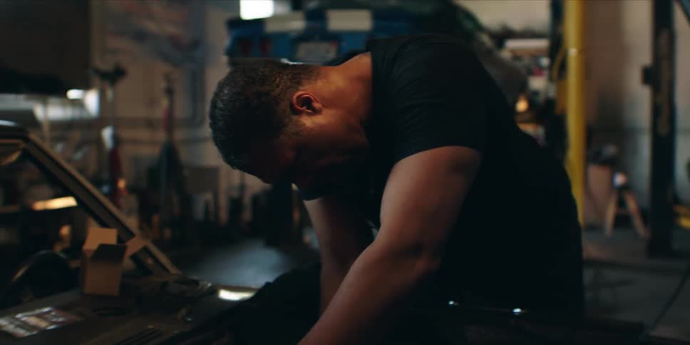 An auto mechanic is fixing something under the hood of a car in a garage