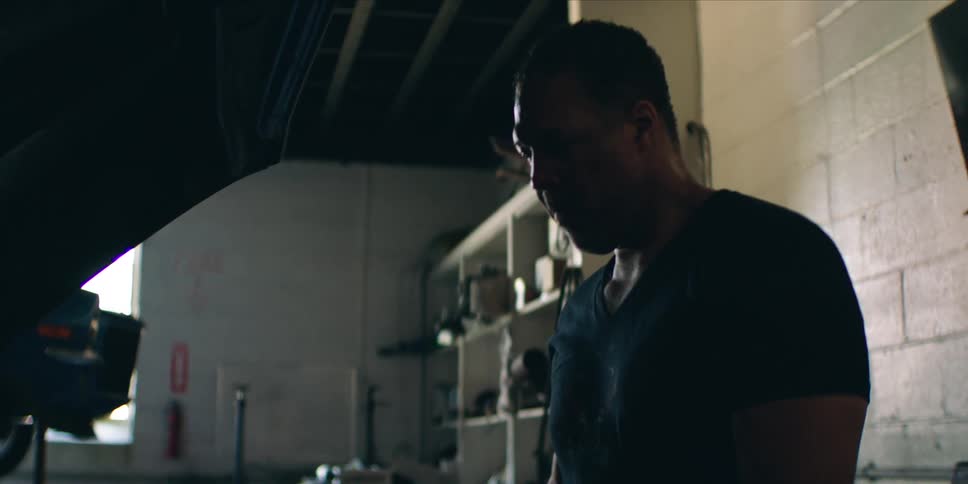 A man works intently under the hood of a car inside a dimly lit garage