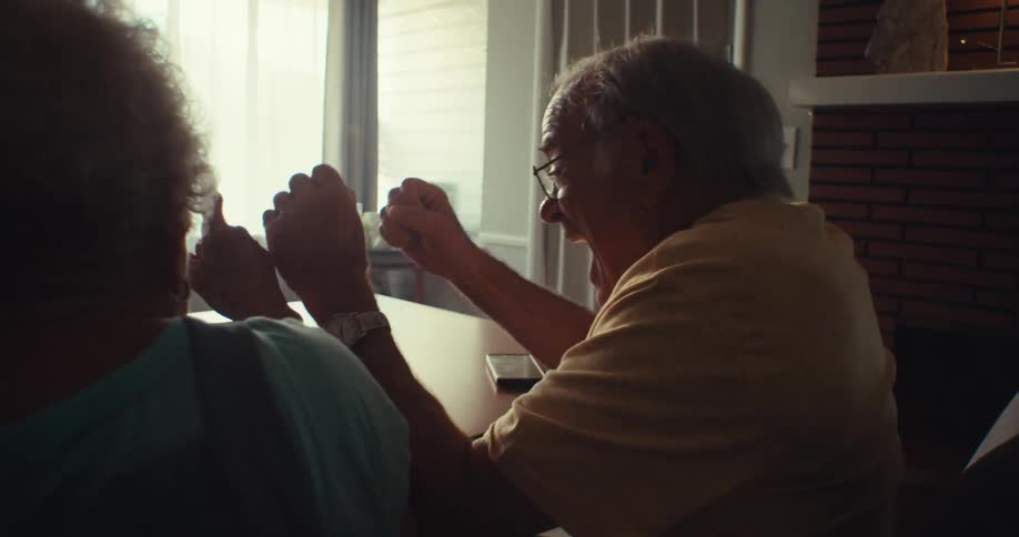 Elderly couple celebrating while watching a basketball game on a tablet at a table in a brightly lit room