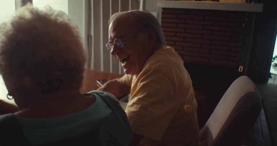 An elderly husband and wife watch something on a tablet and cheer with happiness