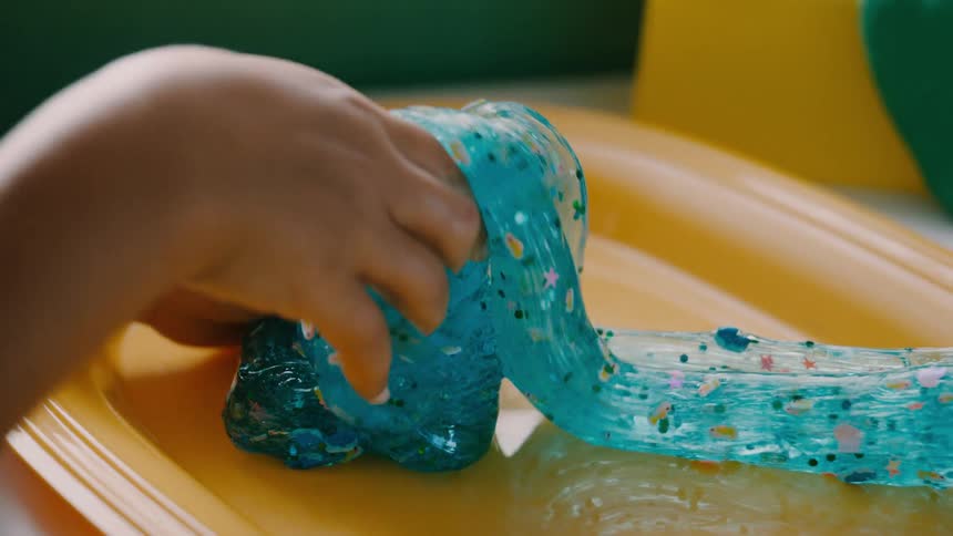 A child plays with sparkly blue slime on a yellow tray