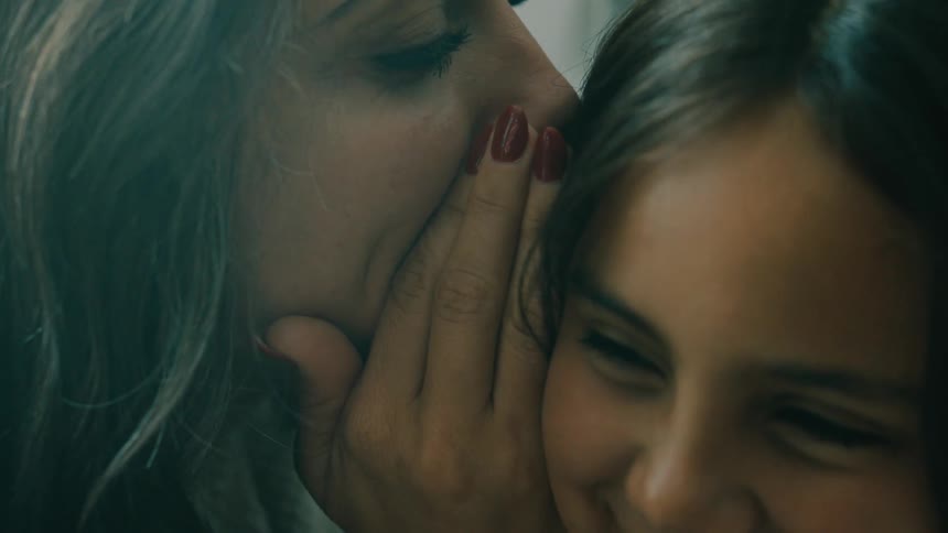 Mother playfully whispers into daughters ear and they both laugh afterwards
