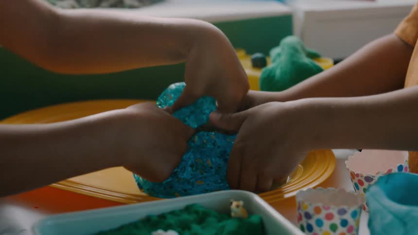 Child sprinkling confetti on transulcent glittered dough then molding it with thier friend