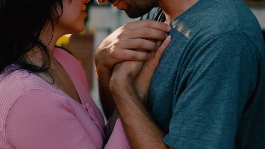 Close up of a couple hold hands while embracing themselves as they stand outdoors during the day