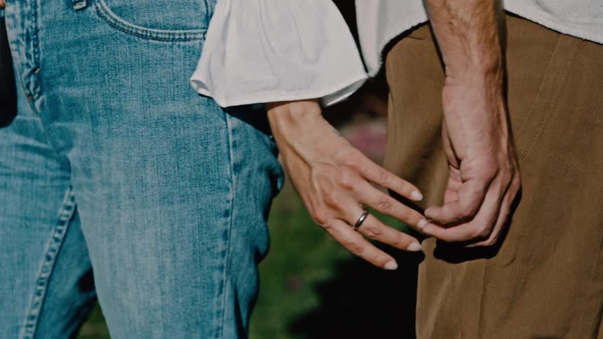 A couple touch hands while standing on the grass
