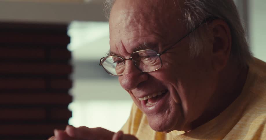 An elderly man smiles and waves enthusiastically during a video call