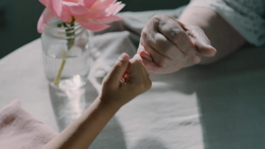 Grandparent and grandchild pinky swear while sitting at a small table
