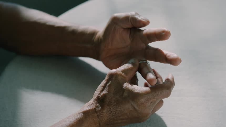 Close up of a man holding and inspecting a ring on a tabletop and wearing it on his ring finger shortly after