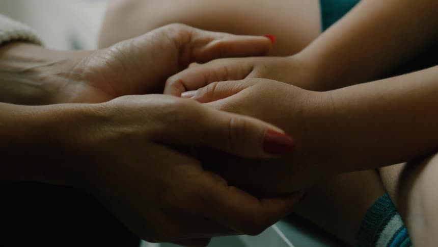 An adults hands are gently holding a childs hands comforting him