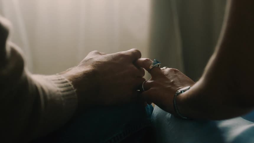 Two people are gently holding hands against a soft sunlit background