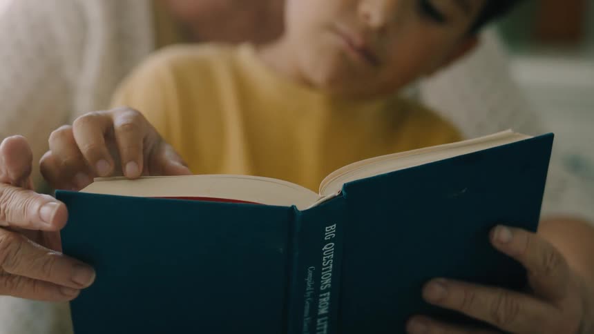 A child and an adult read a book together focusing on their hands and the open book