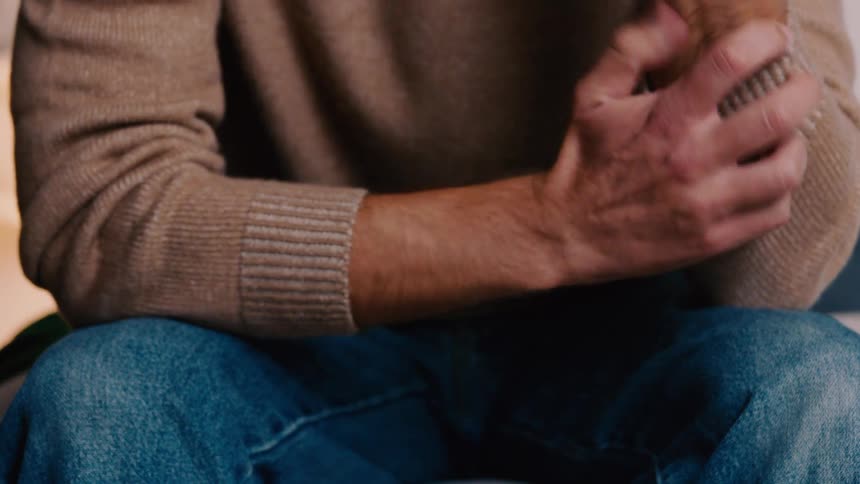 A man rubs his arms and clasps his hands